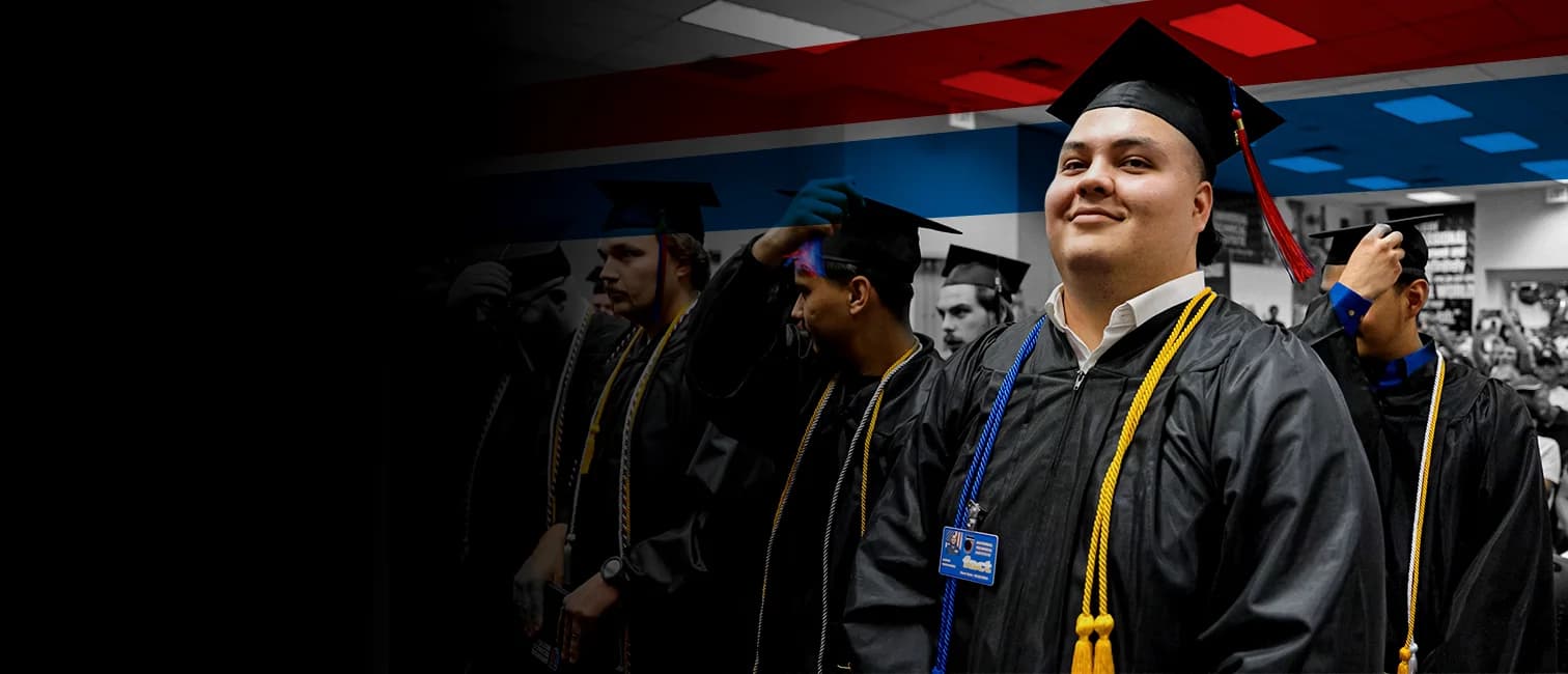 UTI trade school graduate wearing a black cap and gown with honor cords, smiling at commencement ceremony.