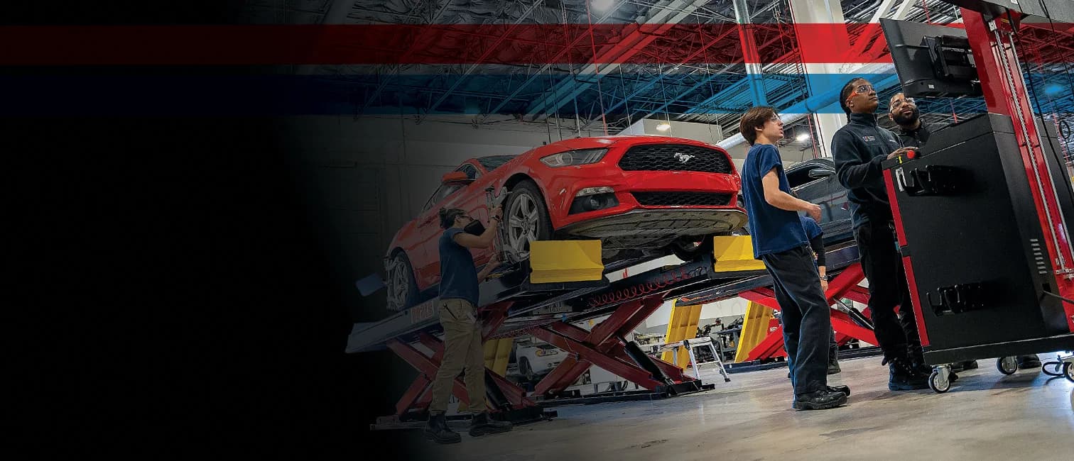 UTI trade school graduate wearing a black cap and gown with honor cords, smiling at commencement ceremony.