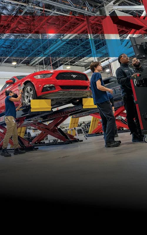 UTI trade school graduate wearing a black cap and gown with honor cords, smiling at commencement ceremony.