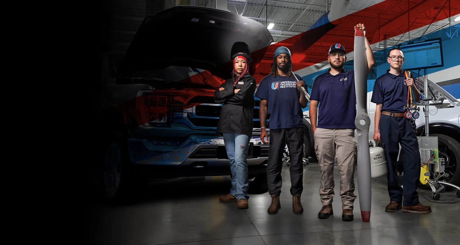Automotive students train in a UTI Auto lab with a red sports car raised on a hydraulic lift behind them.