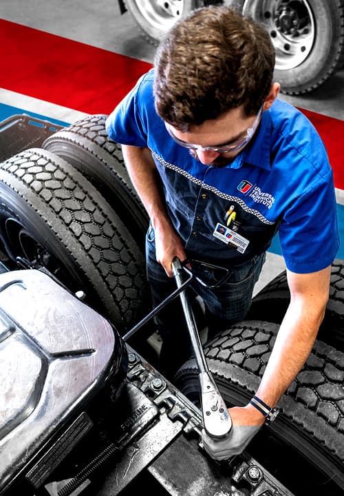 UTI trade school graduate wearing a black cap and gown with honor cords, smiling at commencement ceremony.